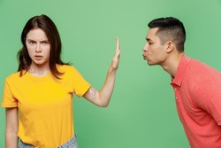 Young couple two friends family man woman wear basic t-shirts together man try want kiss woman but she do stop palm gesture and does not want it isolated on pastel plain light green color background