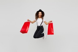 Full body excited jubilant happy young woman wear t-shirt hat hold in hand red paper package bags after shopping jump high isolated on plain solid white background. Black Friday sale buy day concept