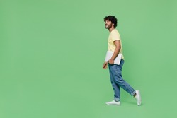 Full body side view young smiling happy fun Indian man 20s in yellow t-shirt hold closed laptop pc computer look aside on workspace mock up walk isolated on plain pastel light green background studio