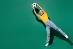 Full body young goalkeeper cheerful woman fan wearing basic yellow t-shirt cheer up support football sport team hold in hand catch soccer ball watch tv live stream isolated on dark green background