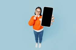 Full body top view from above young woman of Asian ethnicity wear orange sweater glasses hold in hand use mobile cell phone with blank screen area isolated on plain pastel light blue cyan background