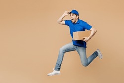 Full body side view delivery guy employee man wear blue cap t-shirt uniform workwear work as dealer courier jump high hold cardboard box run isolated on plain light beige background. Service concept