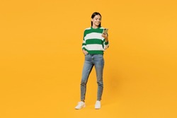 Full body young latin woman wear casual green knitted sweater hold in hand use mobile cell phone chatting online surfing internet isolated on plain yellow background studio People lifestyle concept