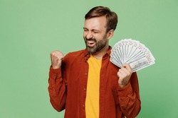 Elderly excited happy man 40s years old he wears casual clothes red shirt t-shirt hold in hand fan of cash money in dollar banknotes do winner gesture isolated on plain pastel light green background