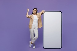Full body overjoyed young latin woman wear light shirt casual clothes big huge blank screen mobile cell phone smartphone with area do winner gesture isolated on plain pastel purple color background