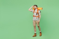 Full body young traveler white man carry backpack stuff mat walk look far away distance isolated on plain green background. Tourist leads active healthy lifestyle. Hiking trek rest travel trip concept