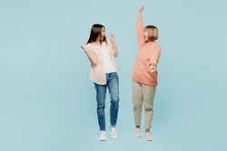 Full body excited elder parent mom with young adult daughter two women together wearing casual clothes raise up hands do winner gesture clench fist isolated on plain blue background Family day concept