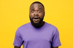Young shocked scared sad man of African American ethnicity he wear casual clothes purple t-shirt look camera with opened mouth isolated on plain yellow background studio portrait. Lifestyle concept
