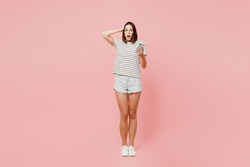 Full body scared sad young astonished caucasian woman she wears casual clothes t-shirt hold head use mobile cell phone isolated on plain pastel light pink background studio portrait. Lifestyle concept