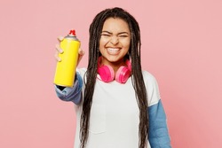 Young woman of African American ethnicity in white sweatshirt casual clothes hold in hand container with spray paint for graffiti stretch hand to camera isolated on plain pastel light pink background