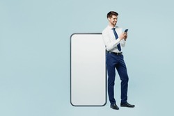 Full body young employee IT business man corporate lawyer in classic formal shirt tie work in office big huge blank screen mobile cell phone with area use smartphone isolated on plain blue background