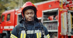 Portrait of african american Firefighter in uniform and helmet near fire engine.