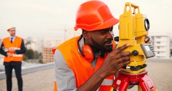 African American young man topographer in casque measuring angle with total station on roof of building. Male builder. Constructor doing topographic measures. Geodesy concept. Geodesy. Constructing.