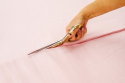 Woman's hand cuts pink fabric with scissors.