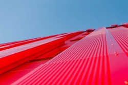 Modern red architectural office building. Metal sheets covering the exterior of the structure. Modern futuristic style building. Clear sky at the background. Unique building.