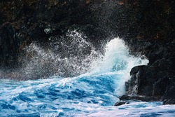 Ocean waves breaking on the black volcanic cliffs, stormy day. Storm season, seascape. Waves breaking on the black rocks