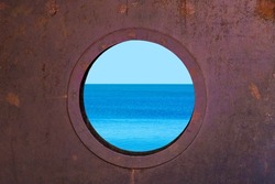 Porthole with ocean view. View of the silent sea surface through a rusty porthole of the ship. Old ship cabin window