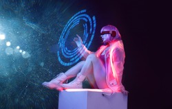 Beautiful woman with purple hair in futuristic costume on dark background. Girl in glasses of virtual reality. Augmented reality game, future technology, AI concept. Holographic interface.