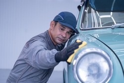 Professional car service male worker, with orbital polisher, polishing green classic vintage car in auto repair polishing shop