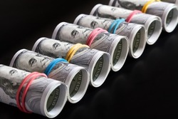 A row of rolled hundred dollar bills with rubber bands on dark background