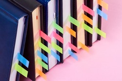 Close-up of a stack of office notepads with colorful sticky page markers sandwiched between pages on pink background