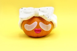 Contemporary art collage. Pumpkin with eye patches. Dressed in a soft plush headband after a shower, on a yellow background. Halloween celebration concept.