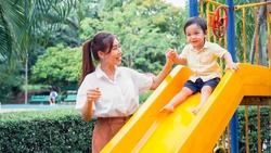 Asian young mother encourage the little boy her by high five before the little son will play slides in the playground.