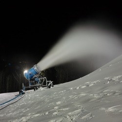 Snow cannon spraying artificial snow on a ski slope, night panorama at long exposure, closeup.