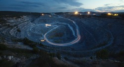 View of the stone quarry after sunset, the sources of electric light from the mining equipment working inside, the glowing traces of passing dump trucks are visible. Night panorama, top view.