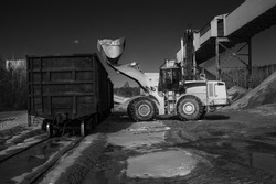 Loading crushed stone into a freight railroad wagon using a front-end loader, at a mining processing factory, black and white.