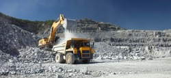 Heavy mining truck and excavator, close-up, against the background of the panorama of a limestone quarry. Long exposure of a moving excavator has a blurred image.