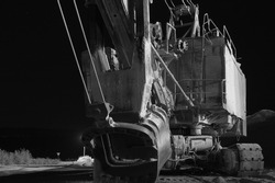 An old worn-out mining excavator abandoned in the open after a stone quarry shut down due to the imposition of economic sanctions. Night black and white image in low key, close-up.