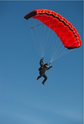 Figure of a parachutist with a bright red parachute against a blue sky.
