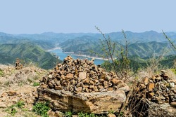 Stacks of small rocks atop large boulder with river in valley in background.