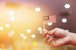 Malaysia Independence Day celebration.Man's hand holding small Malaysian flag with bokeh background.