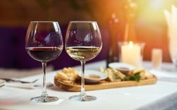 Two glasses of wine white and red standing on a table with candle in the sun light 