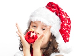 Adorable child wearing Santa Claus hat playing with a Christmas ball