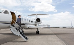 Man standing on the stars of a private jet wearing a hat.