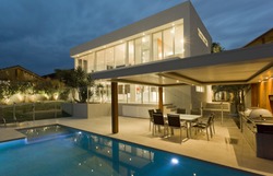 Modern house at dusk with swimming pool and barbecue in backyard 