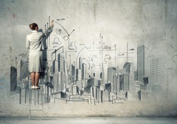 Businesswoman standing on ladder and drawing sketch on wall