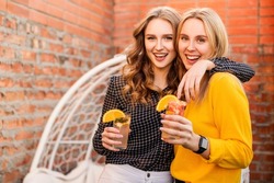 Two young women drinking healthy drinks outdoors. Happy female friends with citrus cocktails on the roof party