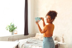 Smiling African American girl stands back to camera in middle of bed room with palette of blue shades for interior renovation, choosing paint for balance of mind and body, refreshing indoor design