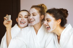 Three young happy women with face masks taking selfi at spa resort. Frenship and wellbeing concept