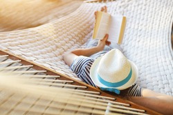 Lazy time. Man in hat in a hammock with book on a summer day