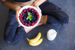 Above shot of a woman with a bowl of berries, a bottle of almond milk and two bananas wearing a sportive outfit.