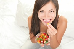 Candy woman eating sweets with a fresh smile in bed - copy space. Top view of Mixed Chinese Asian / Caucasian young female model.