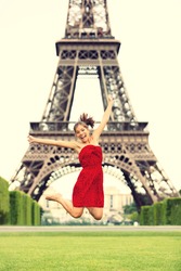 Paris girl at Eiffel Tower jumping happy smiling excited in red summer dress. Joyful young woman on Champs cheerful during vacation / holidays in Paris, France, Europe.