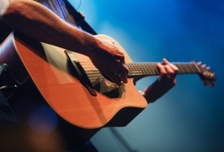 Professional musician plays acoustic guitar solo on concert stage in music hall.Analog audio equipment in close up.Retro style sring musical instrument on rock and roll festival in nightclub.