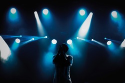 Cool young rap singer with microphone on bright backlit stage in bright blue lights.Hip hop star performing solo set on scene in music hall.Popular rapper sings a song on rock festival in nightclub