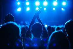 Silhouette of music fan clapping hands on concert in night club. Happy young woman enjoying the show in music hall. Blue musical festival background with group of cheerful fans